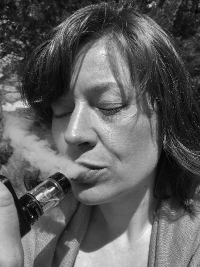 A woman vaping nicotine from a tank with her eyes closed.