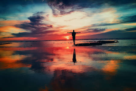 A person standing on the beach during sunset with his arms stretched wide.