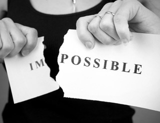 Lady holding and ripping a piece of paper on which the word impossible was written so as to make a new word: possible