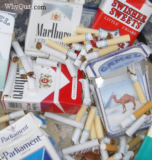Photo showing broken cigarettes and cigarette packs in a sand ashtray.