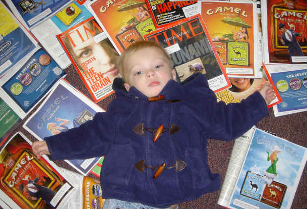 Photograph of a young boy laying among Time magazines containing cigarette and tobacco advertisements.