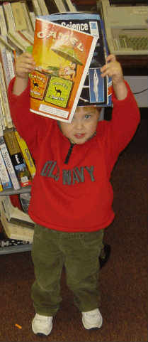 A young boy holding up a copy of Popular Science opened to a page displaying a Camel cigarette advertisement