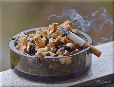 A full ashtray and a burning cigarete
