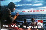 PMI advertisement stating 'Be the dream, be Marlboro. The ad shows a young male in a sailor's skull cap holding a lit cigarette while gazing out at the ocean from what appears to be a boat, while a couple in front and below him gaze out at the ocean too.