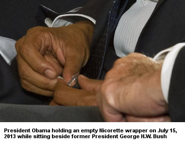 President Obama holding an empty Nicorette wrapper while sitting next to former President George H.W. Bush on July 15, 2013