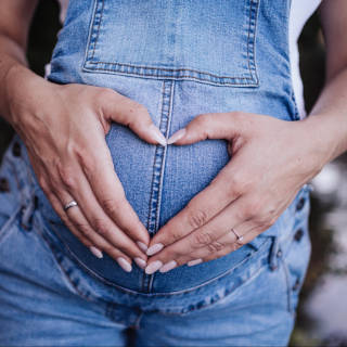 Picture of a pregnant woman in overalls making a hands heart over her tummy